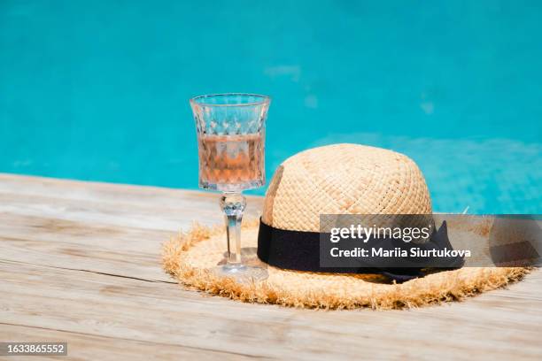 rose wine in a crystal glass and beautiful straw hat by the swimming pool. - drinkwater kante stock-fotos und bilder