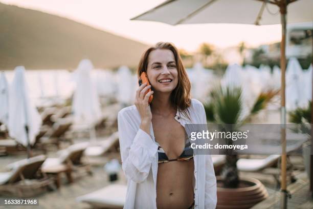 young woman talking on a smartphone at the beach on a sunny summer day - young woman beach stockfoto's en -beelden