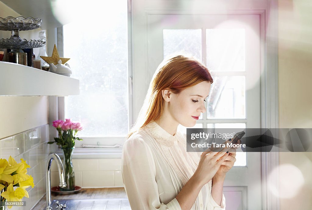 Woman texting on mobile in kitchen