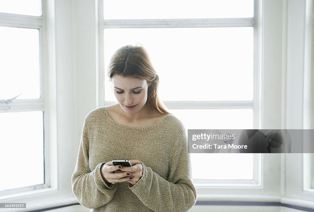 Woman looking at mobile phone by window
