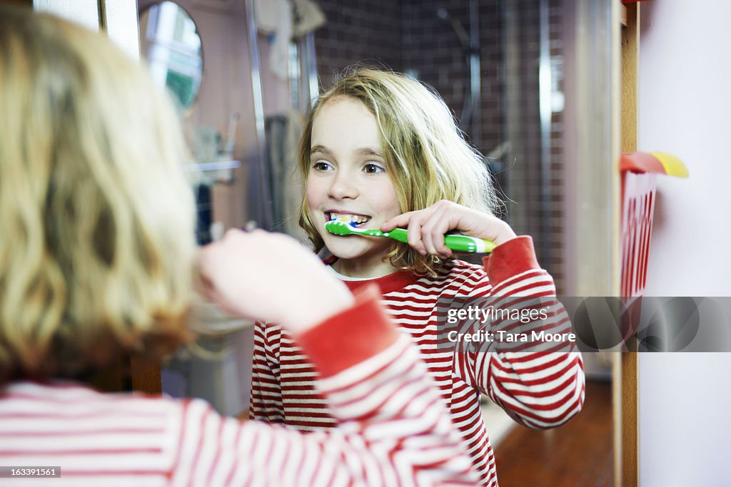 Young girl brushing teeth in bathroom mirror