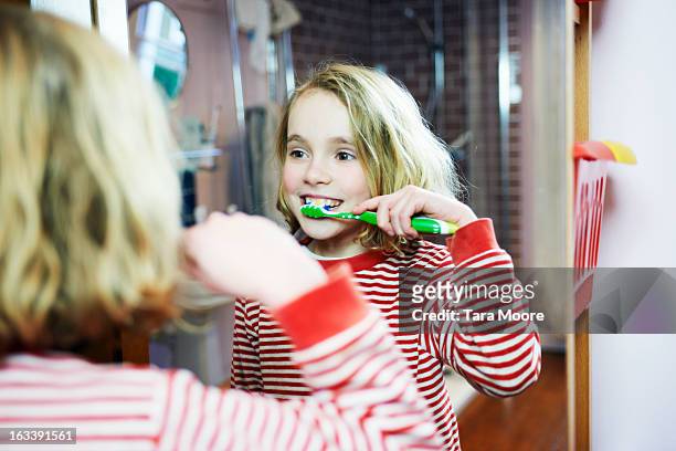 young girl brushing teeth in bathroom mirror