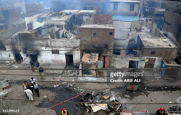 Pakistani police officials examine the burnt out houses of members of the Christian community attacked by Muslim demonstrators during a protest over...
