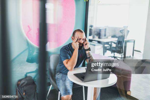 tired computer programmer sitting in coworking at the table with laptop - shorts stock pictures, royalty-free photos & images