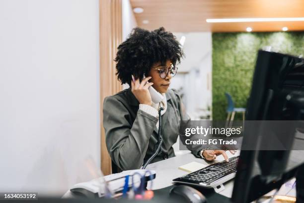 receptionist young woman talking on landline phone in the medical clinic - service occupation stock pictures, royalty-free photos & images