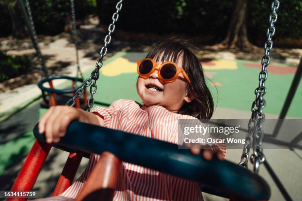 cute asian little girl with sun glasses playing on swing in the playground - altalena foto e immagini stock