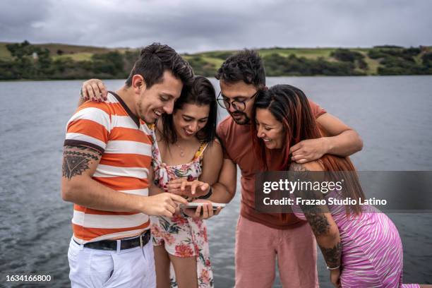 young man showing something on mobile phone to his friends on the beach - colombia beach stock pictures, royalty-free photos & images