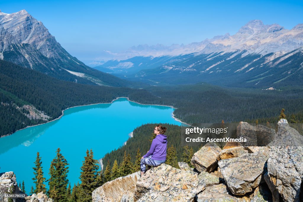 Woman relaxes above Peyto Lake, looks off to view