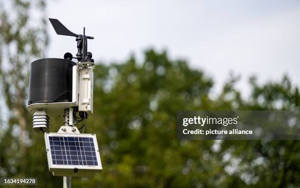 August 2023, Lower Saxony, Adendorf: A weather station complete with rain gauge stands on a golf course. The image of golfers and their clubs is...