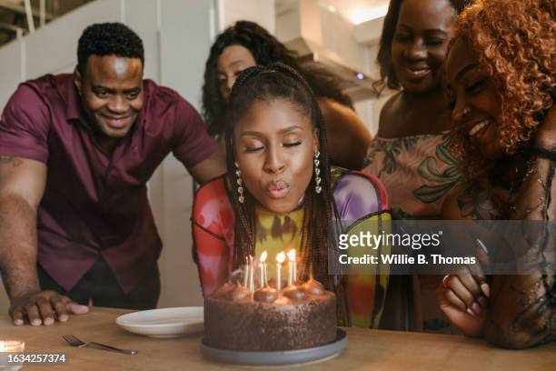 a woman blowing out candles on her birthday cake during party - exhale stock pictures, royalty-free photos & images