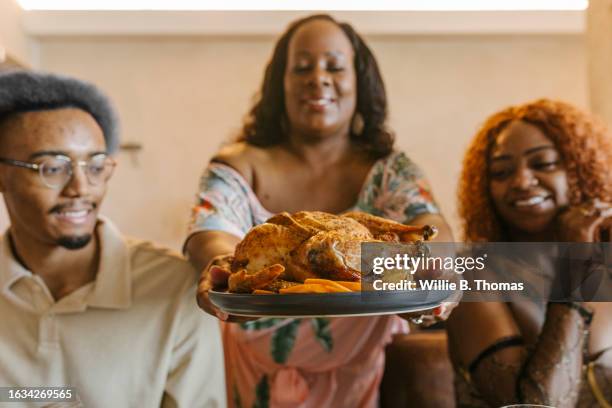 woman bringing roast chicken to table during dinner party - afroamerikansk kultur bildbanksfoton och bilder