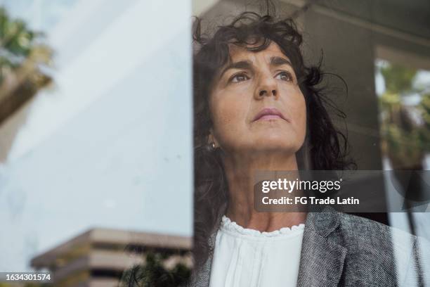 mature businesswoman contemplating and looking through the window at office - anxiety stock pictures, royalty-free photos & images