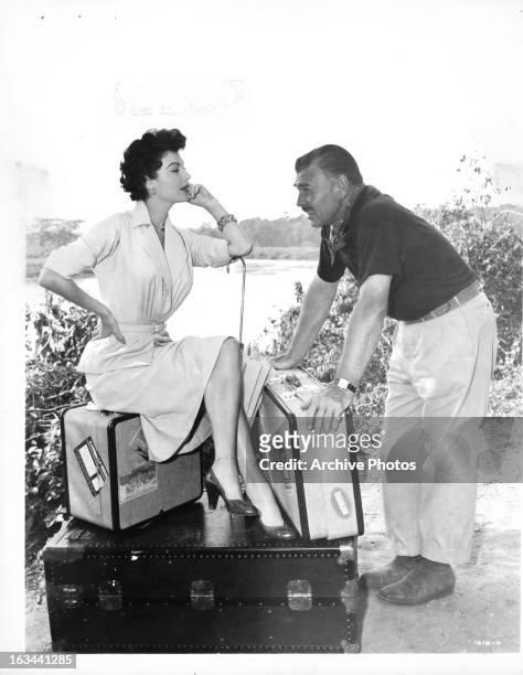Ava Gardner sitting on luggage in front of Clark Gable in a scene from the film 'Mogambo', 1953.
