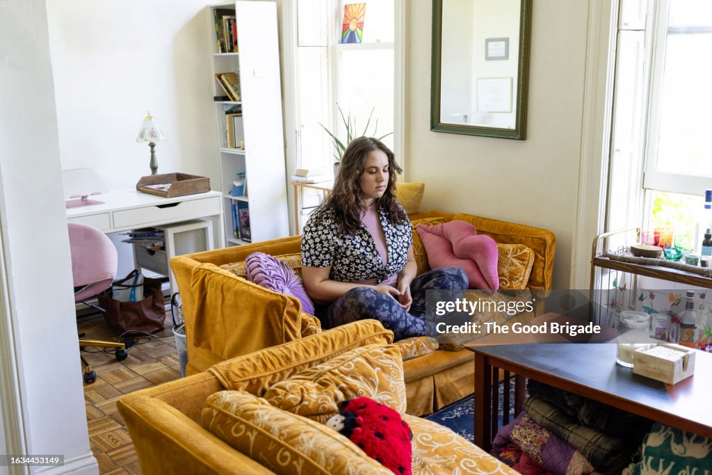 Young woman meditating on sofa at home