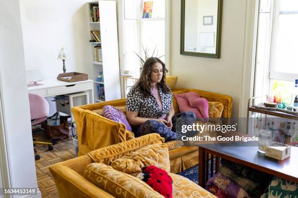 young woman meditating on sofa at home - studio apartment stock pictures, royalty-free photos & images