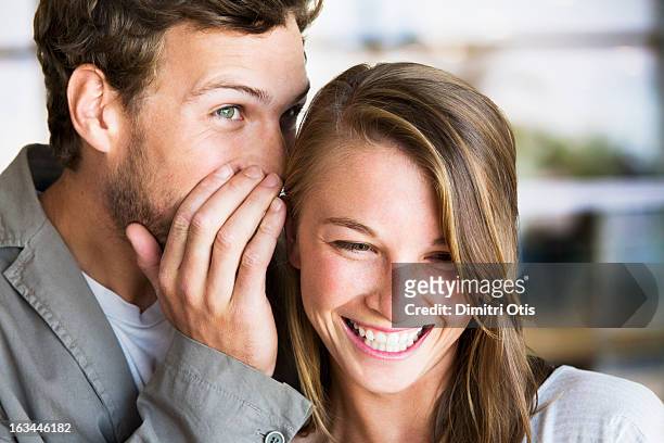 young man whispers into young woman's ear - gossip stockfoto's en -beelden