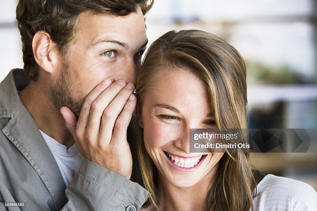 Young man whispers into young woman's ear