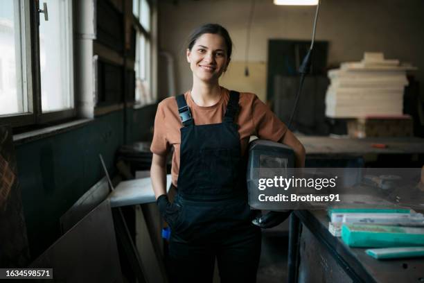 portrait of a young woman welder at metal workshop - empreiteiro de reparações imagens e fotografias de stock
