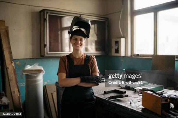 portrait of a profession female welder with welding helmet on head at workshop - construction worker pose stock pictures, royalty-free photos & images