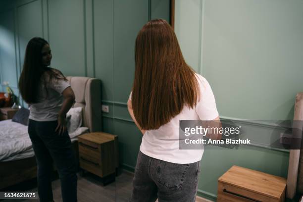 young woman looking at her reflection in mirror at home - human build stock pictures, royalty-free photos & images