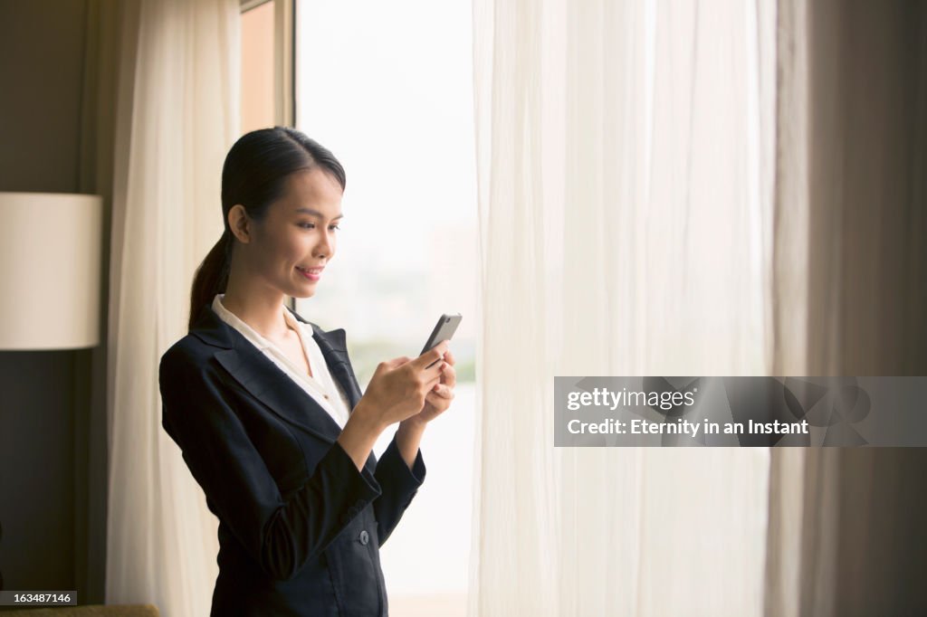 Businesswoman using smartphone in front of window