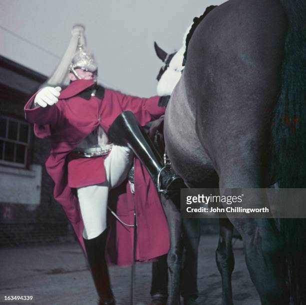 Trooper Campbell, of the Life Guards, mounts his horse at Hyde Park Barracks, Knightsbridge, London, May 1953. Original publication: Picture Post -...