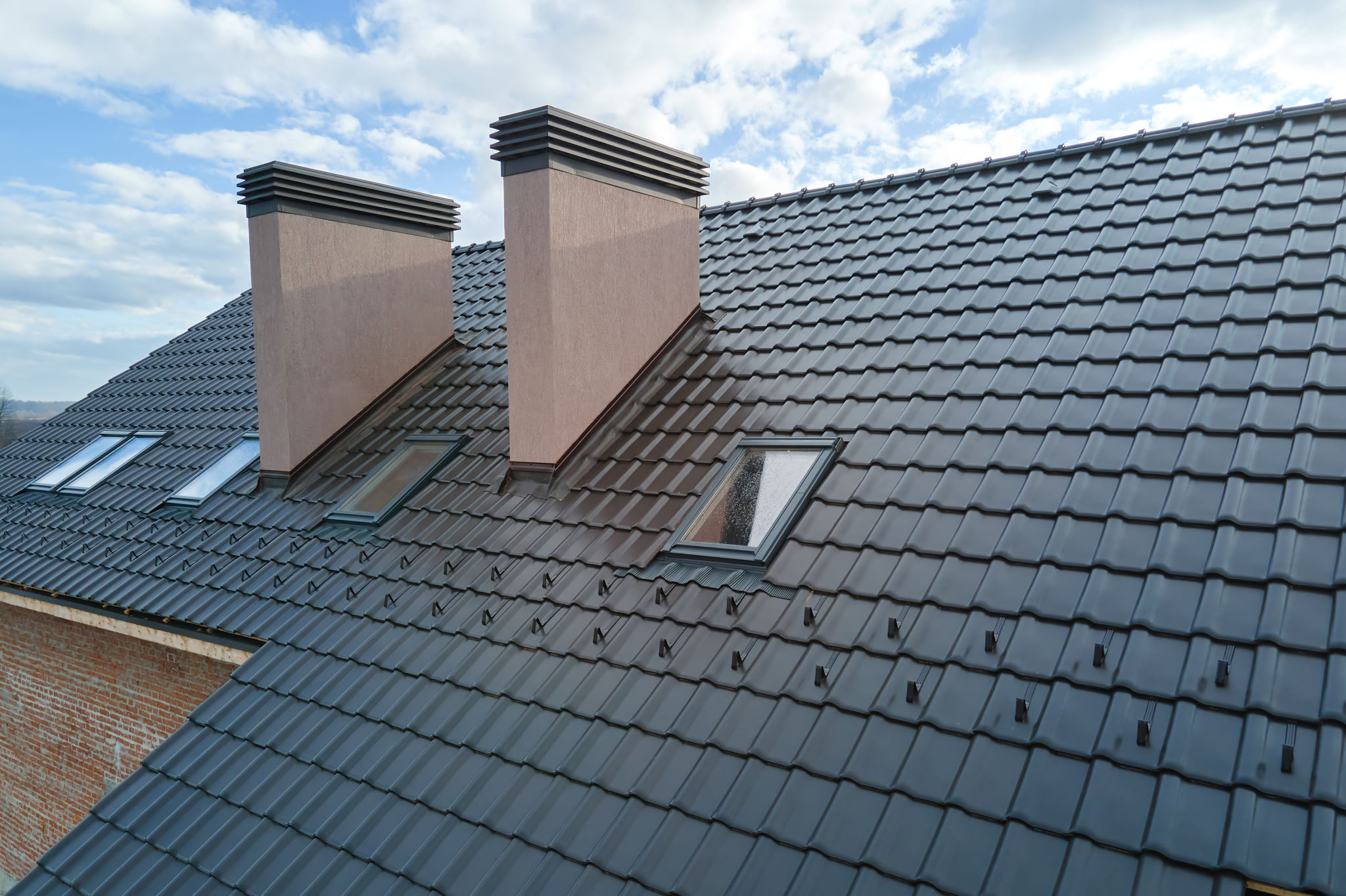 Closeup of attic windows and brick chimneys on house roof top covered with ceramic shingles. Tiled covering of building Closeup of attic windows and brick chimneys on house roof top covered with ceramic shingles. Tiled covering of building