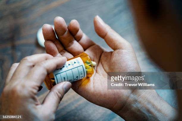 close-up of a male hand holding a pill bottle pouring medication into his hand - prescription drug stock pictures, royalty-free photos & images