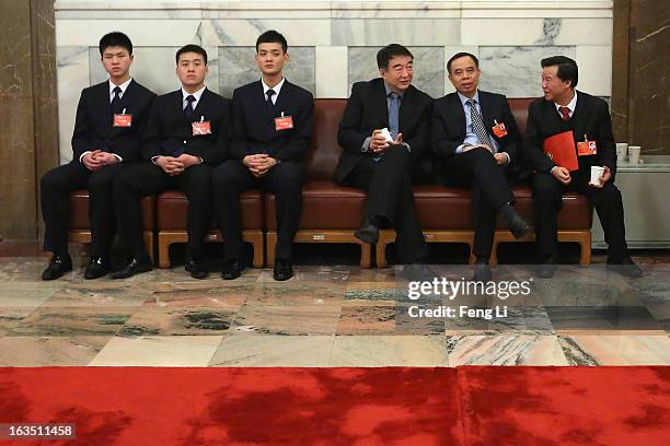 Three delegates talk outside the meeting room as three security personnel guarding during the plenary session of the Chinese People's Political...