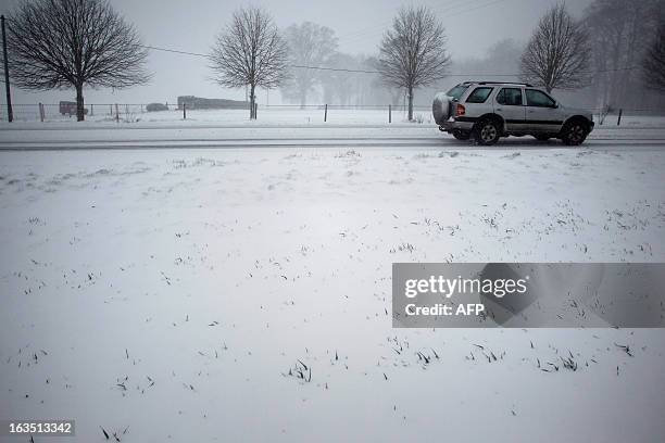 Picture taken on March 11, 2013 in Routot, northwestern France shows a car driving under snow falls. AFP PHOTO/CHARLY TRIBALLEAU.