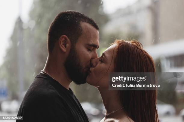 charming young couple kisses passionately while standing on street under summer downpour - couples kissing shower photos et images de collection