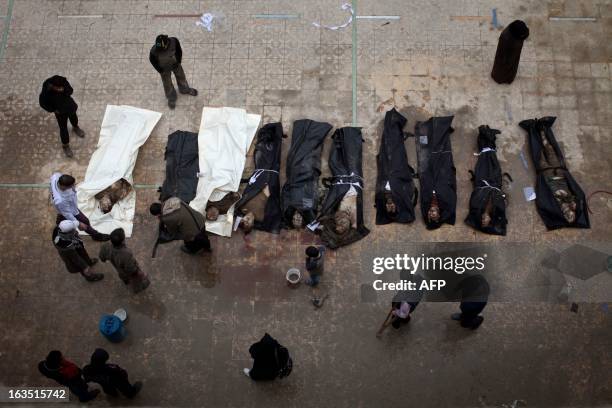 Syrian men search for their relatives amongst the bodies of civilians executed and dumped in the Quweiq river, in the grounds of the courtyard of the...