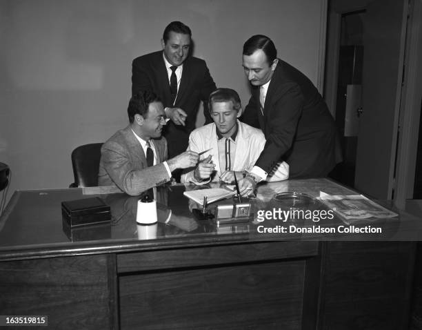 Disc jockey and promoter Alan Freed hands a pen to rock and roll musician Jerry Lee Lewis as Milt Shaw and Freed's business manager Jack Hook look on...