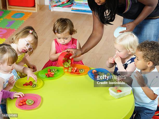 carer serving fruit to group of toddlers/ children at nursery - babysit stockfoto's en -beelden