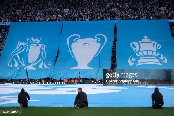 Manchester City fans unvweil a banner with the three trophies from their treble winning season before the Premier League match between Manchester...