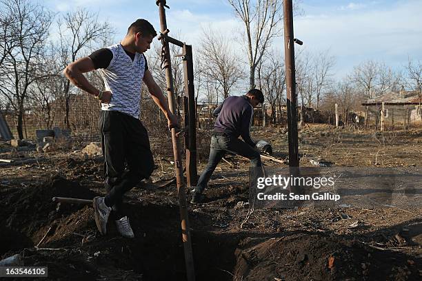 Ethnic Roma Costin Costea and his brother Florin dig out iron columns that were part of a shed to make way for a vegetable garden on the property of...