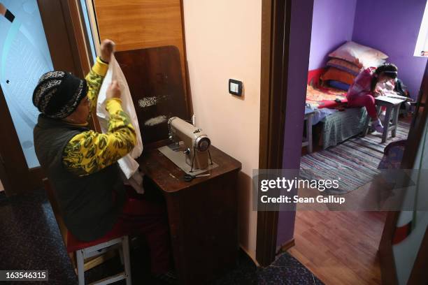 Aneta Enache, an ethnic Roma, works at her sewing machine while her grandaughter Madelina does her English homework in the living room on March 11,...