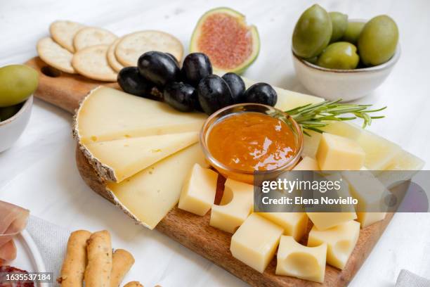 cheese board with different types of hard cheeses with grapes and jam and crackers, an appetizer for dinner or aperitifs - gouda cheese stock pictures, royalty-free photos & images