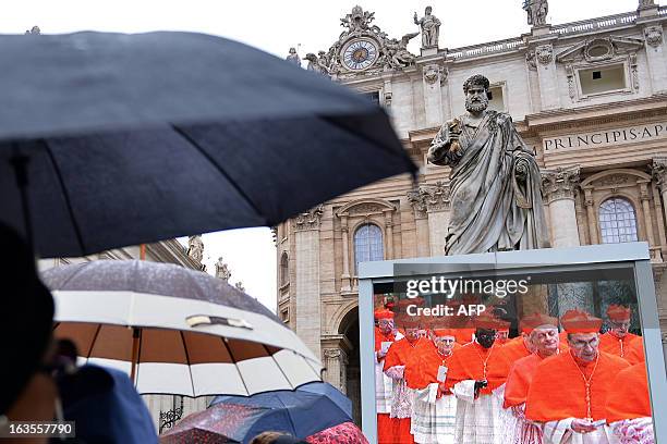 Faithful, holding umbrellas, look at a giant screen, setup under a statue of St Peter, showing the start of the papal election conclave on St Peter's...