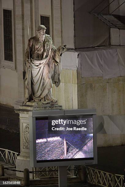 Television screen setup in St. Peters Square shows black smoke billowing from the chimney on the roof of the Sistine Chapel indicating that the...