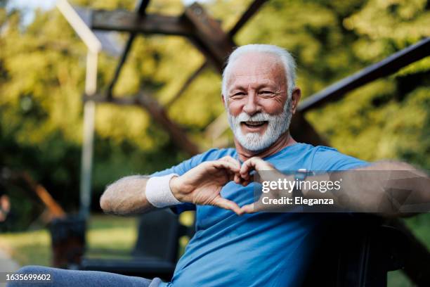 portrait of a senior sporty man in nature showing a heart-shaped symbol - menselijk hart stockfoto's en -beelden