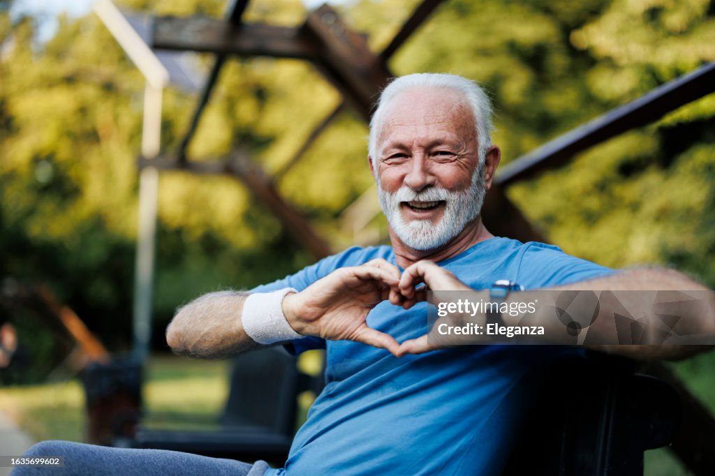 Portrait of a senior sporty man in nature showing a heart-shaped symbol