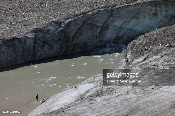 Hiker stands in front of the collapsing face of the Pasterze, Austria's biggest glacier, and a river of meltwater at the end of the glacier tongue on...