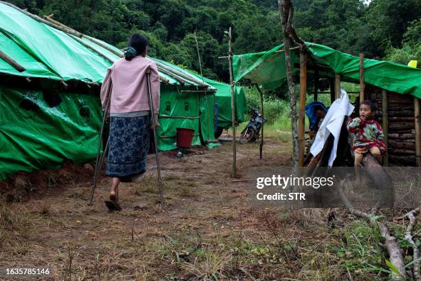 In this photo taken on July 29, 2023 Hla Win walks with crutches near her son at an internally displaced people camp near Pekon township. Myanmar's...