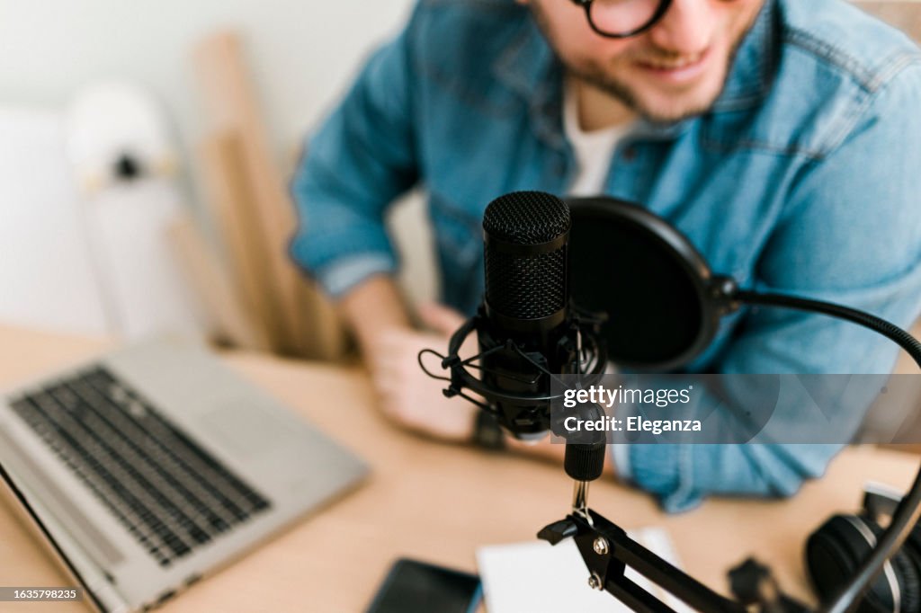 ポッドキャストを録音し、レコーディングスタジオでマイクとヘッドフォンを使用してライブストリーミングを行う若い笑顔の男性の接写