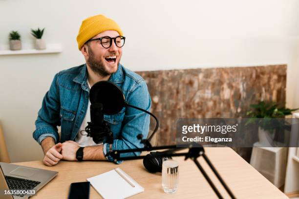 young smiling man recording podcast and doing live streaming using microphone and headphones in recording studio - commentator imagens e fotografias de stock