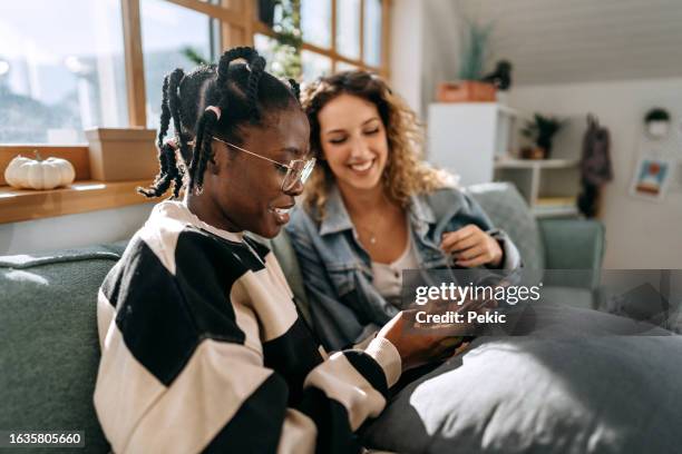 dos jóvenes estudiantes vestidas casualmente usando el teléfono en casa - compañero de vivienda fotografías e imágenes de stock