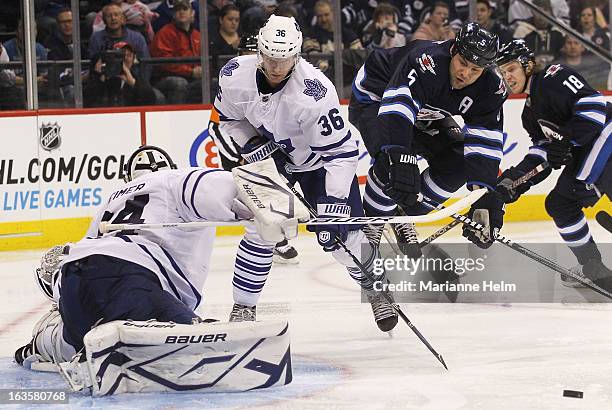 Carl Gunnarsson of the Toronto Maple Leafs watches as Mark Stuart of the Winnipeg Jets jumps into the air to miss the puck during a shot on goal...