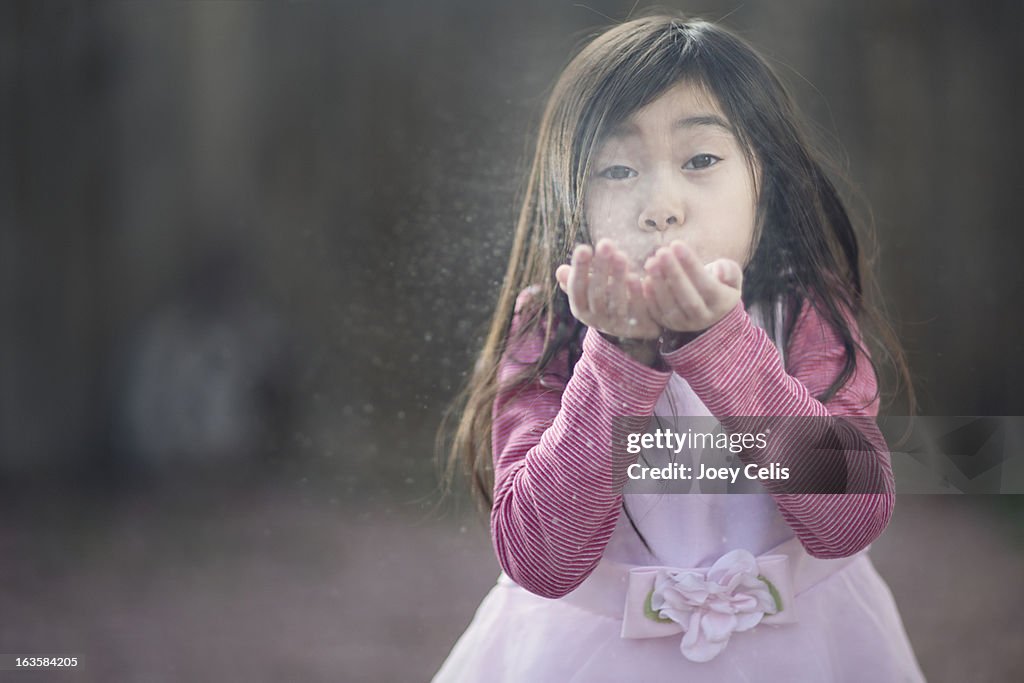 Asian girl in pink dress blows sand from her hands