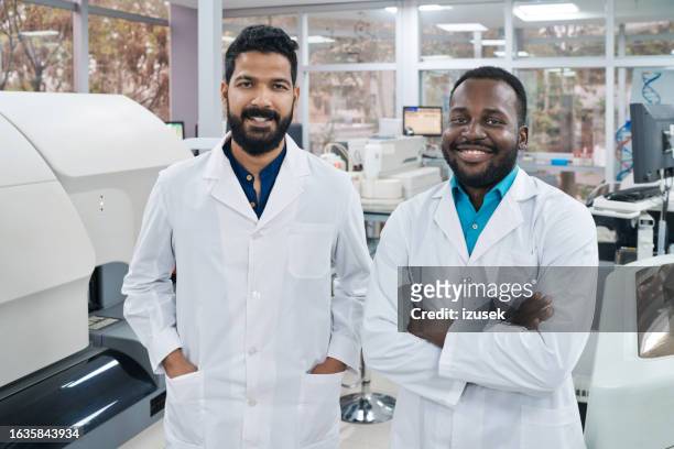 portrait of smiling male scientists standing together in laboratory - young man scientist stock pictures, royalty-free photos & images